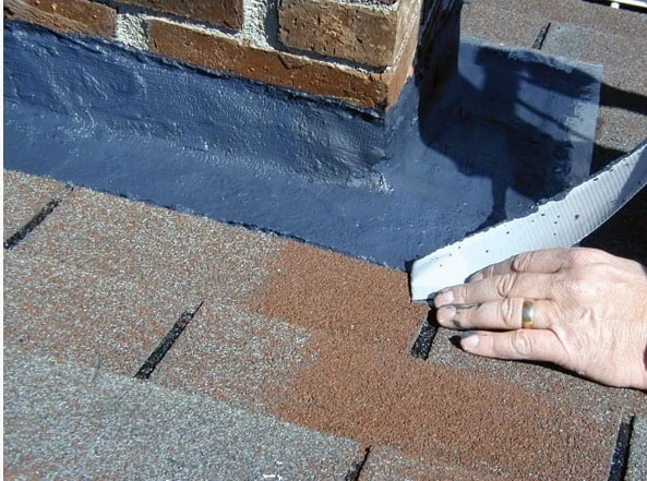 Roofing sealant being applied around the flashing at the base of a brick chimney